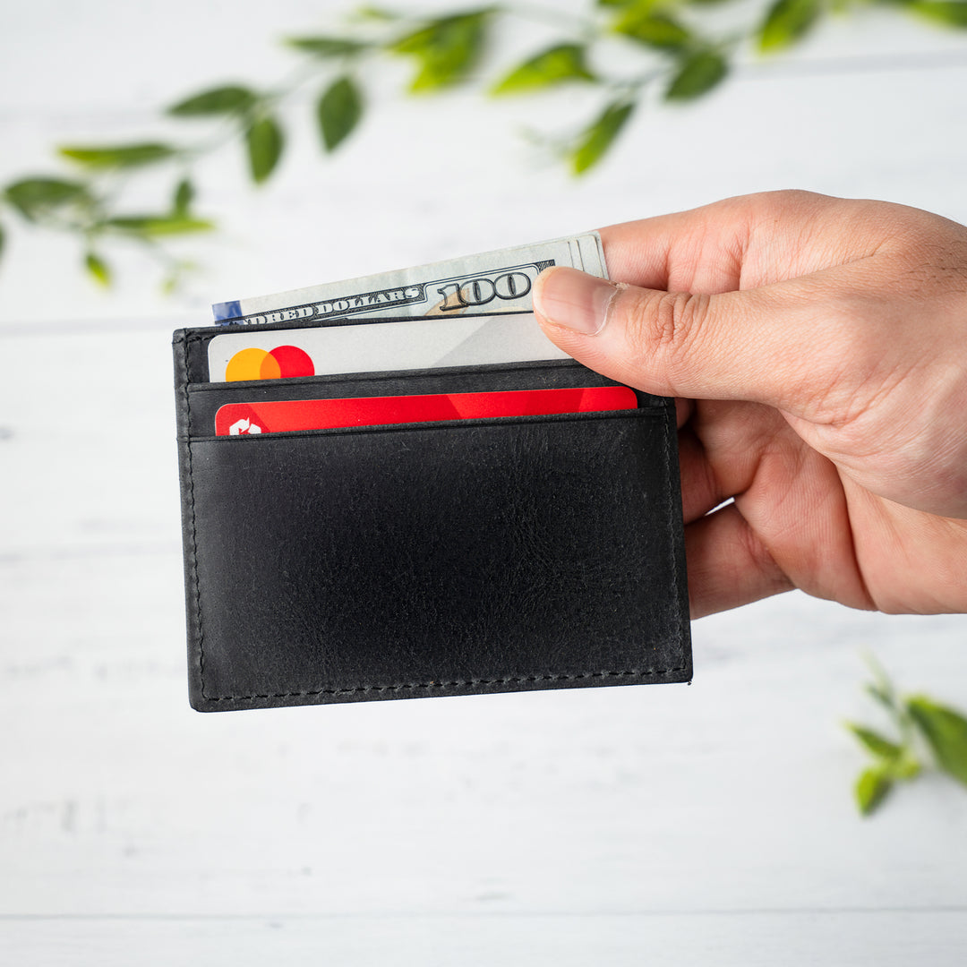 Hand holding a black wallet with cards against a light background