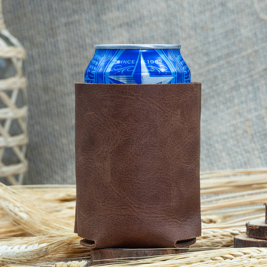 Brown leather can cooler with a blue can inside, placed on a rustic background.
