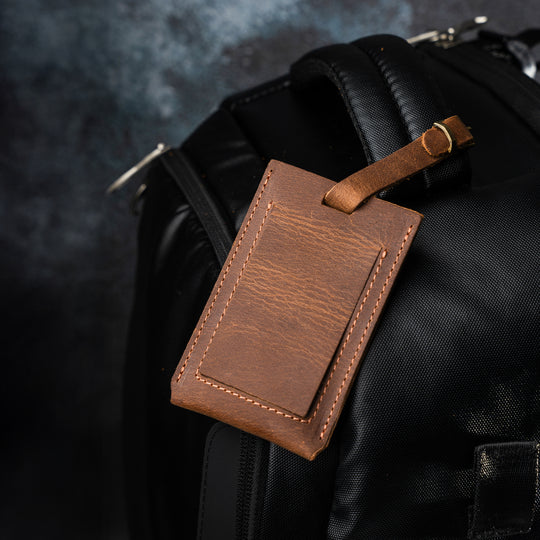 Brown leather luggage tag attached to a black bag with a dark background