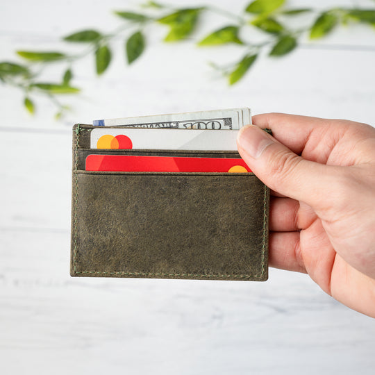 Hand holding a green wallet with cards against a light background