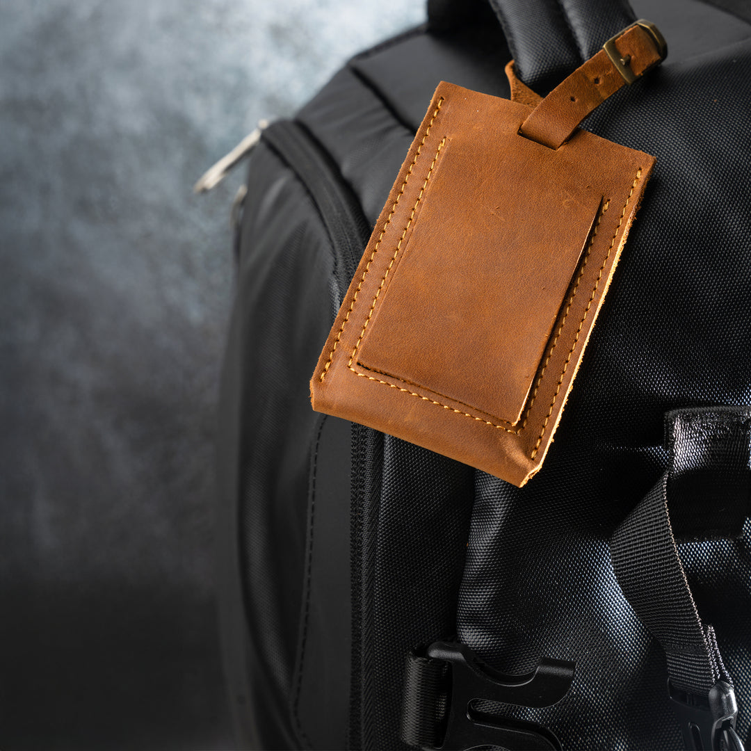 Brown leather luggage tag attached to a black backpack on a blurred gray background