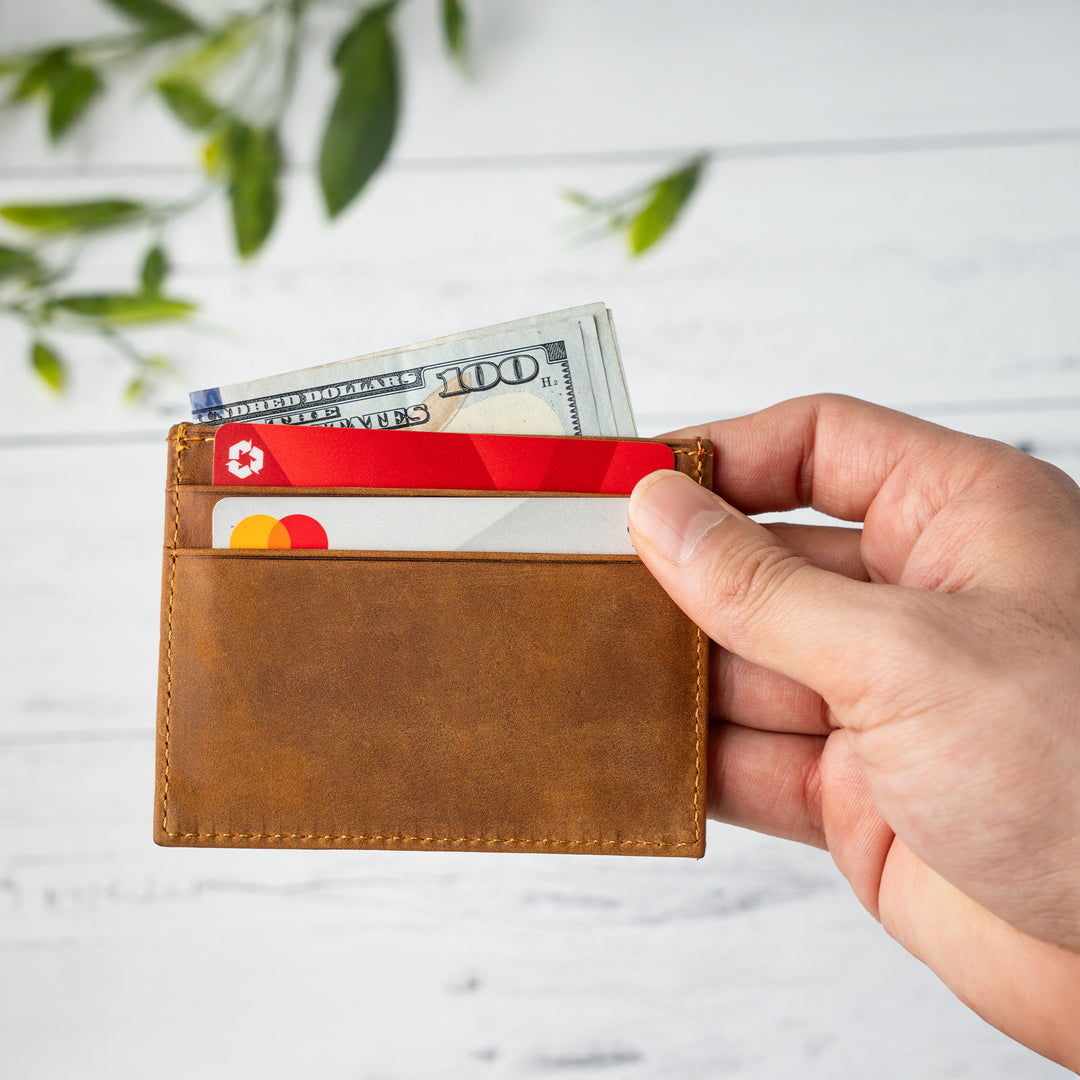 Person holding a brown leather wallet with money and cards against a light background