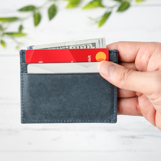 Hand holding a blue cardholder with a red card and money against a light background